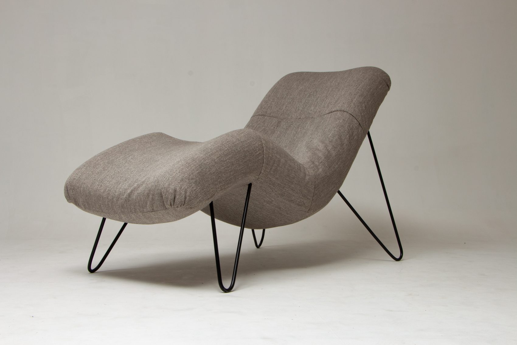 Assise CAP’EMI vue de trois quarts : une forme ondulée, garnie de tissu chiné gris, sur des pieds en métal noir
