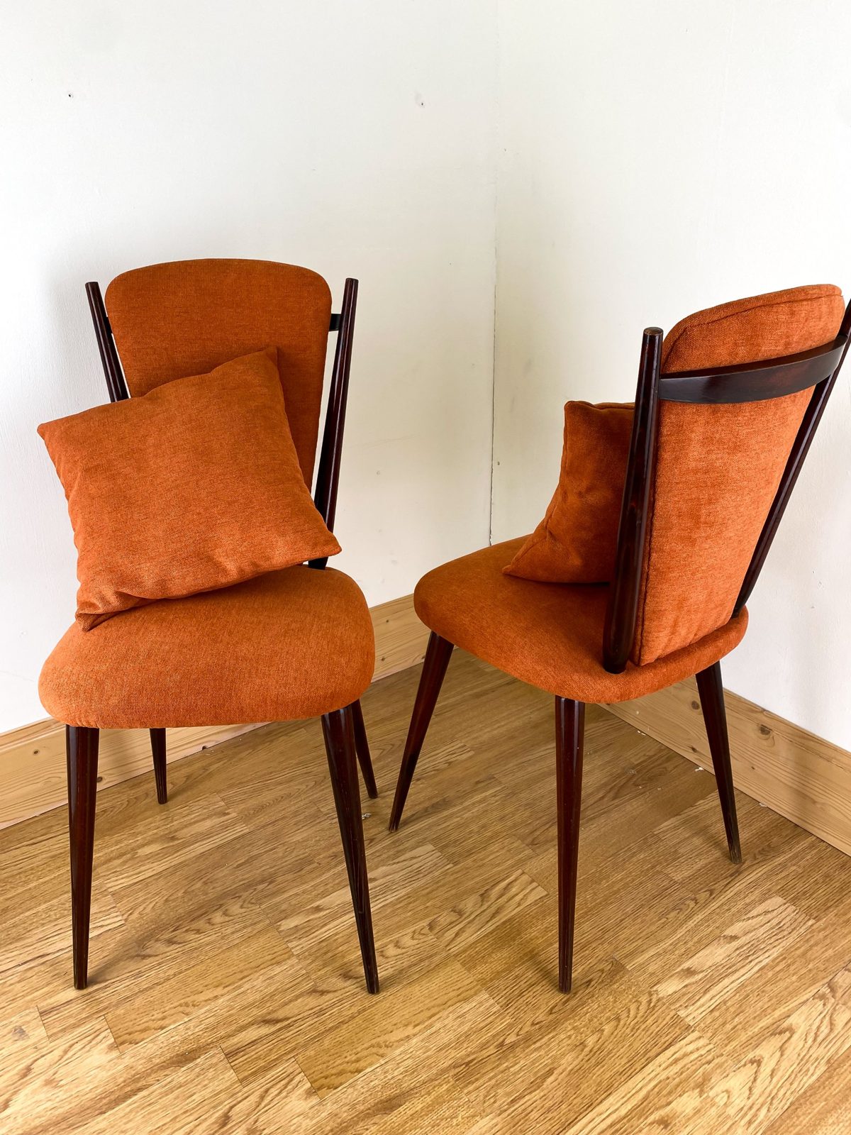 Réfection de chaises : deux chaises vintage en bois foncé recouvertes d’un tissu orange, avec coussins assortis