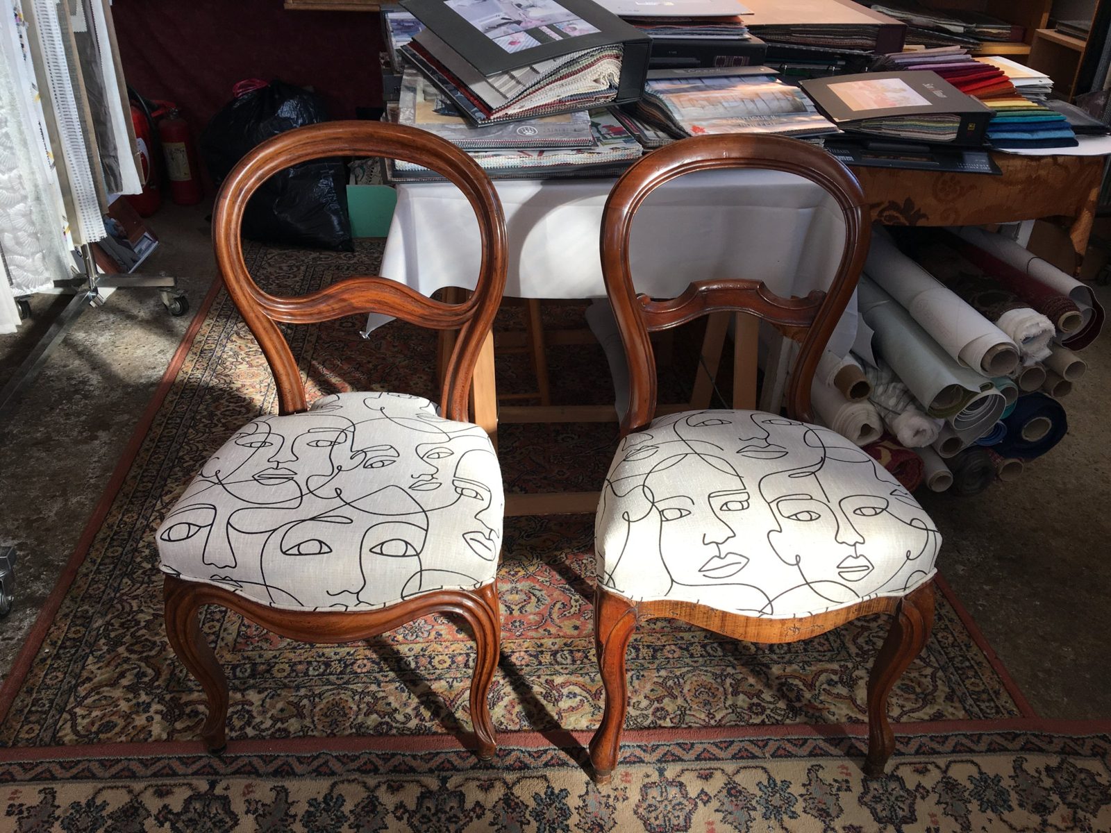 Réfection de chaises : deux chaises à dossier médaillon recouvertes d’un tissu clair orné de visages dessinés au trait